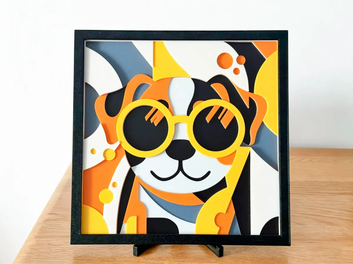 Cool Dog with Glasses layered art: a smiling dog in round yellow glasses on orange, yellow, grey and white shapes, in a black frame on a stand
