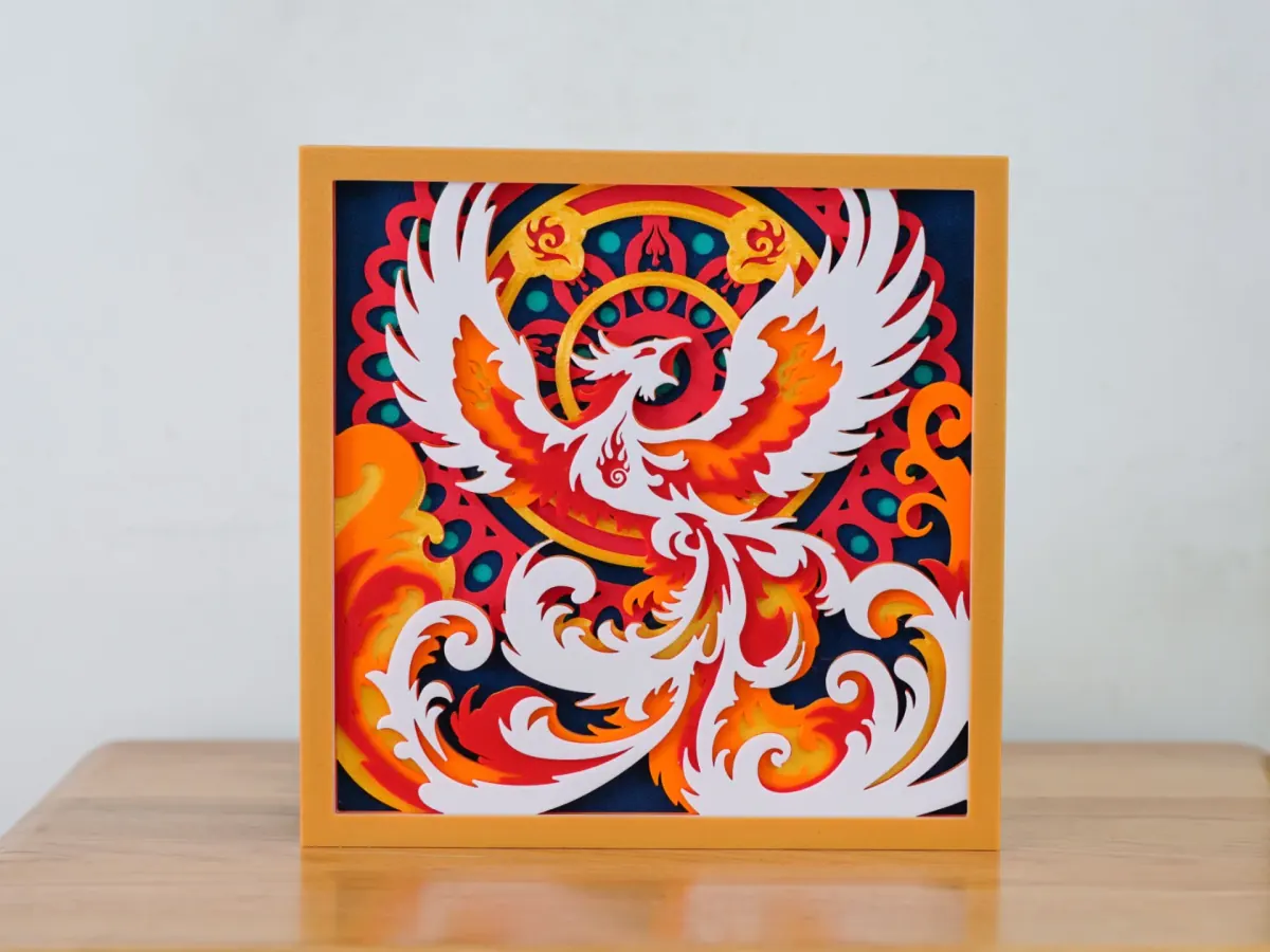 Fire Phoenix layered art: a white phoenix with spread wings and orange flames in front of a red and navy mandala, in a golden frame